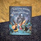 „Three Little Witches and the Spooky Old House“. Drei Hexen vor einem alten Haus, Fledermäuse und eine Eule sind zu sehen.