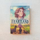 „Heartland“, Jilanne Hoffmann. Eine Illustration mit einer Frau im Vordergrund, einem Bauernhof, einem Pferd und einem Hund.