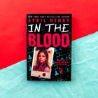 Buchtitel: "IN THE BLOOD" von April Henry. Foto einer jungen Frau, rote und blaue Hintergründe mit Blutflecken.