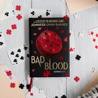 Der Text "BAD BLOOD" dominiert, mit "Jennifer Lynn Barnes" darüber. Spielkarten und Puzzlestücke sind verstreut.