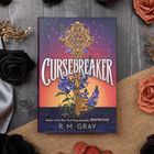 "Cursebreaker" von R.M. Gray. Bunte Buchillustration mit einem verzierten Stab und blauen Blumen. Umgeben von Stoff und Rosen.