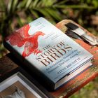 Ein Buch mit rotem Vogel und dem Titel „The Story of Birds“ liegt auf einer Bank. Daneben sind Federn und ein Schädel in einem Rahmen.