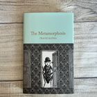 "Oberer Text: The Metamorphosis. Darunter: Franz Kafka. Illustration: Käfer in einem Türrahmen mit einem Menschenkopf."