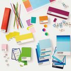 "Pantone Memory Game", "Pantone Charades", "Pantone Dominoes". Bunte Spieleboxen, Karten und Stäbchen auf weißem Hintergrund.