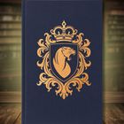 Ein blaues Buch mit einem goldenen, verzierten Wappen, das einen Löwenkopf und eine Krone zeigt. Im Hintergrund sind Bücherregale.