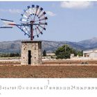 "Wasserrad", "CASARES EDITION", Monatskalender mit einem Bild eines alten, bemalten Windrads auf einem Feld vor Bergkulisse.