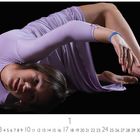 Zahlen 1-31 unten in einer Linie. Person in fließendem, lilafarbenem Kleid macht eine akrobatische Pose auf schwarzem Hintergrund.