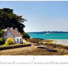 "Morbihan" am unteren Rand. Ein Steinhaus steht am Meeresufer, umgeben von Bäumen und Booten, unter blauem Himmel.