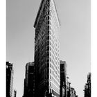 "Flat Iron" steht unter einem spitz zulaufenden Gebäude, das im klassischen Stil erbaut ist.