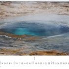 Strokkur Geysir, darunter Kalendertage und Casares Edition. Eine dampfende Wasserquelle mit bläulichem Zentrum.