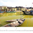 Text: "Hoi An", "1", "2 3 4 5 6 7 8 9 10 11 12 13 14 15 16 17 18 19 20 21 22 23 24 25 26 27 28 29 30 31". 

Szene: Gelbe Häuser am Flussufer, Boote auf dem Wasser.