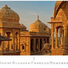 Text: "Bada Bagh Tempel". Sandfarbene, reich verzierte Kuppelbauten mit Säulen in der Abendsonne. Arabisches Design.
