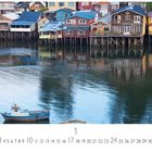 „Castro, Chiloé Insel“ steht über einem Kalenderblatt. Farbige Häuser auf Stelzen spiegeln sich im Wasser. Ein Boot liegt im Vordergrund.