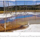 "Yellowstone Nationalpark". Eine heiße Quelle mit blauen und orangefarbenen Tönen, umgeben von kahlen Bäumen.