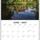 Juni 2027 Kalender, ländliches Haus am ruhigen See, umgeben von Bäumen unter blauem Himmel.