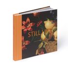 „STILL LIFE“ in Orangetönen, daneben Blumen und Früchte, darunter ein Korb, Buch mit orangefarbenem Rücken.
