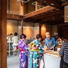 Oben rechts: Menü mit Kaffeevarianten. Zwei Frauen in bunten Kimonos bestellen an einer Theke in einem Café aus Holz.