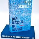 Cover eines Buches mit blauem, texturiertem Hintergrund. Aufschrift: "INGO SCHULZE DAS WASSER IM AUGUST ROMAN."