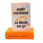 Cover von "Die Unruhe der Zeit" von Audrey Niffenegger. Blumenmuster, Buch liegt auf orangefarbenem Exemplar.