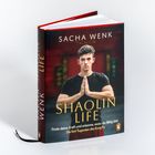 Vorwort – Baoquanli. Ein Mann sitzt mit verschränkten Armen in roter Hose vor einem Tor mit asiatischer Architektur.