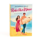 "KATHERINE REILLY, Ride the Wave, Line-up für die Liebe, Roman. Ein Paar am Strand, Mann mit Surfbrett, Frau im roten Kleid."