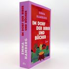 Text: "IM DORF DER BIBER UND BÜCHER" von "EMMA HAMBERG". Illustratives Cover mit Dorf, Häusern und Baumstumpf.