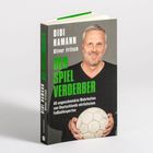 „Didi Hamann, Oliver Fritsch, Der Spielverderber“. Ein Mann hält einen alten Fußball, lächelt in dunklem Hintergrund.