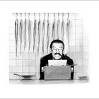 Eine Illustration zeigt einen Mann mit Pfeife vor einer Schreibmaschine, hinter ihm hängen mehrere Fische an Fliesen.