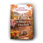 "GITTA EDELMANN, Wenn das Glück in Blättern raschelt, ROMAN." Ein Igel sitzt auf einem herbstlich dekorierten Tisch.