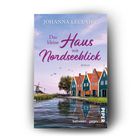 "Johanna Leclaire, Das kleine Haus mit Nordseeblick, Roman." Bunte Häuser am Wasser mit Segelschiff und Baum im Hintergrund.