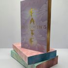 Der Text "SARA WEST FATE BLOOMING ROMAN" ziert ein Buch mit lila Cover, Teil eines bunten Bücherstapels.