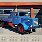 04/2027 Vintage Trucks Calendar. Ein blauer, klassischer Lastwagen vor einer Garage.