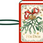 „Für Dich“ ist auf einem Buchumschlag mit Mistelzweig, Glocken und roter Schleife zu sehen.
