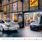 Der Raum zeigt zwei Autos. An der Backsteinwand hängen Vintage-Schilder, darunter "Mobil", "Shell" und "Dunlop".