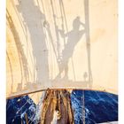 Datum: 01. Ein Schatten fällt auf ein Segel. Ansicht von oben auf ein Segelschiff, umgeben von blauem Meer.