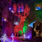 Leuchtender roter Hirsch aus Lichterketten in einer steinernen Ruine, umgeben von bunten Leuchtfiguren und Sternen.