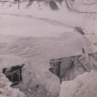 Ich kann den Text nicht lesen. Ein zugeschneites Haus und Bäume am Hügel, alles in dickem Schnee. Ein Zug ist oben sichtbar.