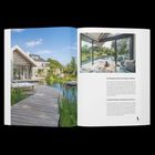 Text: „Ein Übergang zwischen Architektur und Natur“. Zeitschrift zeigt modernes Haus am Wasser mit Holzterrasse und Garten.