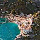 Keine erkennbaren Texte. Küstenstadt an steilen Hängen, azurblaues Meer, bunte Häuser, grüne Terrassen.