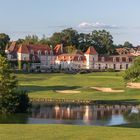 Keine Texte. Ein elegantes Schloss mit roten Dächern, umgeben von grünen Wiesen und einem Teich im Vordergrund.