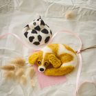 Gefilzte Kuh und Hund auf zerknittertem Papier, daneben rosa Band und getrocknete Gräser.