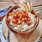 Kein Text vorhanden. Eine hölzerne Schüssel mit Haferbrei, belegt mit gewürfeltem, gewürztem Obst und Apfelscheiben.