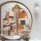 Eine bunte, gesteppte Patchwork-Weste hängt vor einem runden Spiegel; daneben moderne Wandleuchten.