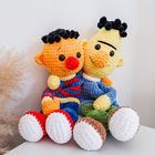 Zwei bunte gehäkelte Puppen sitzen zusammen auf einer weißen Oberfläche, eine gelb, die andere orange.