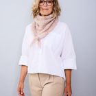 Eine Frau mit blonden Haaren trägt eine Brille, ein weißes Hemd und einen rosafarbenen Schal. Sie lächelt leicht.