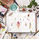 Notizbuch mit botanischen Zeichnungen und Farbmuster. Wasserfarben, Pinsel, Beeren und ein Zweig liegen verstreut.