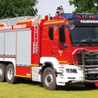 "FEUERWEHR WIESMOOR" und "FEUERWEHR" auf einem roten Feuerwehrauto auf grünem Gras, Bäume im Hintergrund.