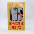 OLIVIA HADDON, DIESE SACHE MIT UNS. Gelber Hintergrund, Illustration: Frau sitzt in einer Küche auf der Arbeitsfläche.