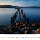 Januar 2024, Montag mit dem 1. beginnend. Alte Holzpfähle führen ins ruhige Wasser, Gebirge im Hintergrund, Sonnenuntergang.