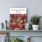 "Literaturkalender Kunst 2024" steht oben. Darunter ein Gemälde mit bunten Häusern. Auf einem Regal sind Kräuter und eine Tasse.